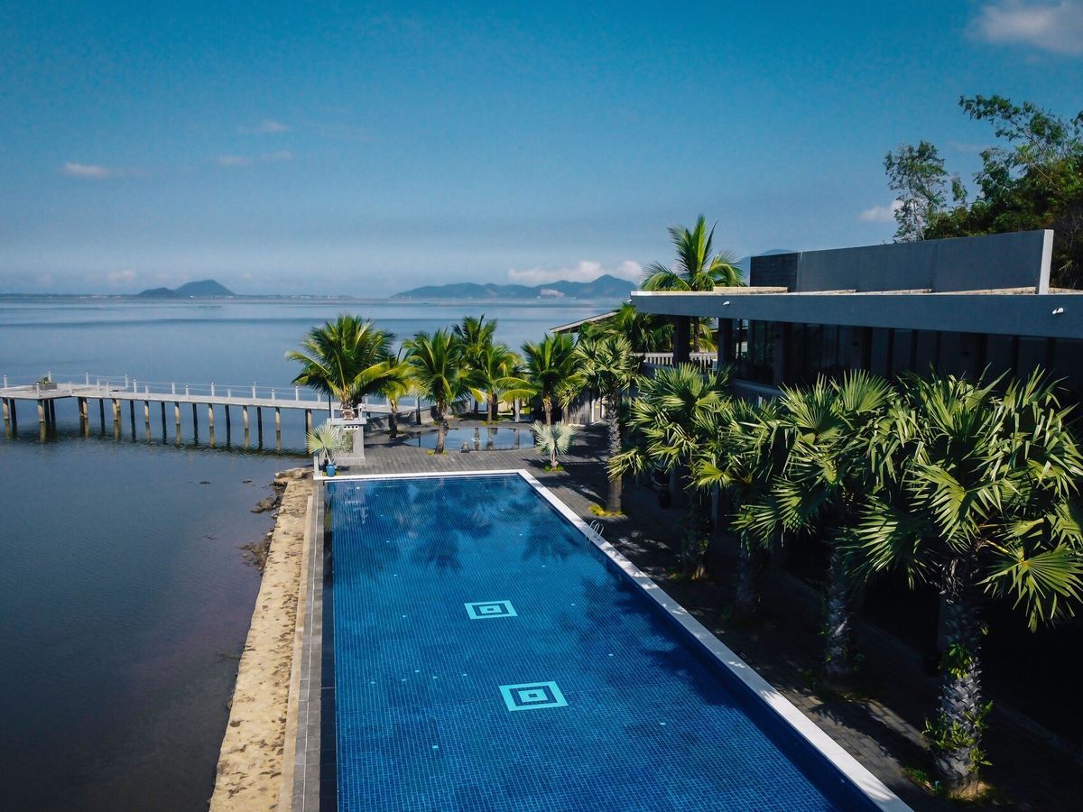 Villa with a long dark-tiled pool running along the lagoon shore, palms and distant islands
