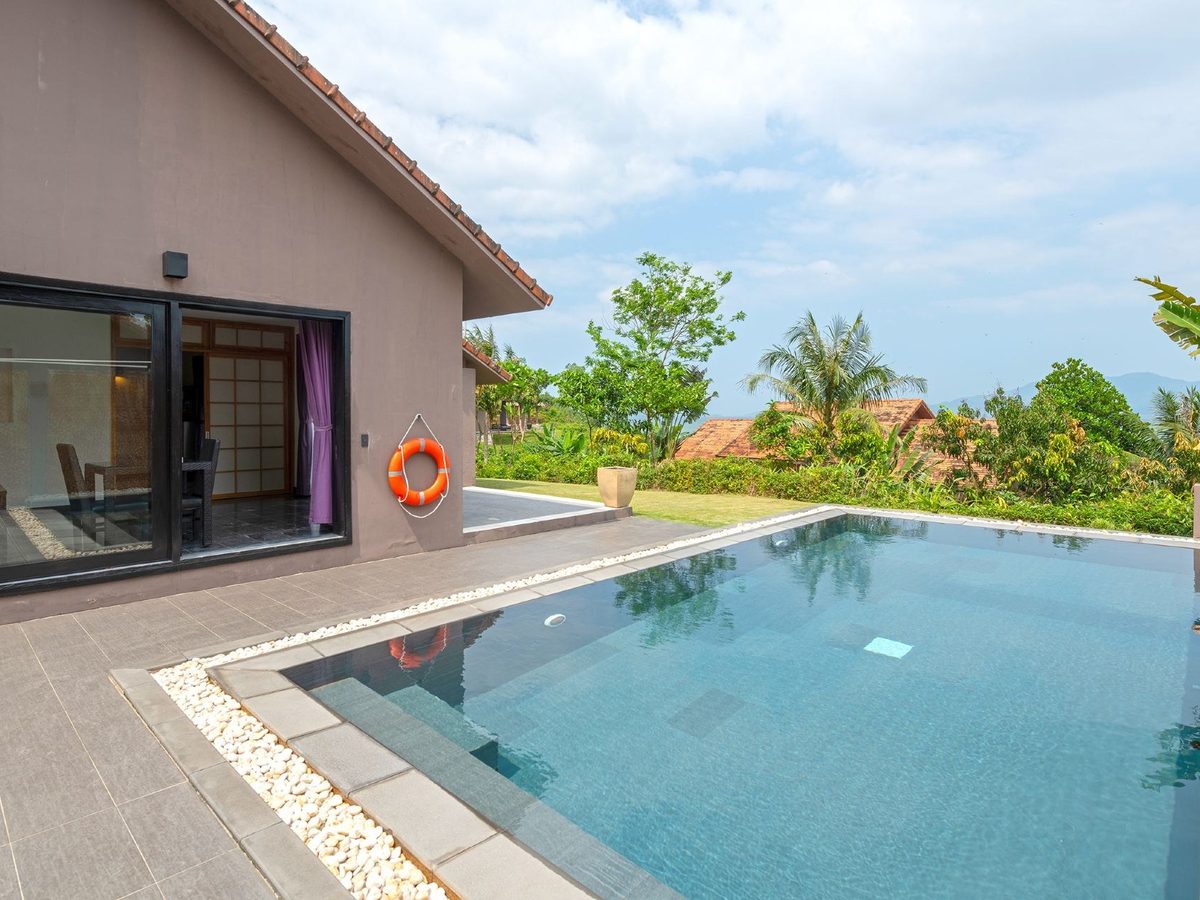 Private pool on a stone terrace beside a tile-roofed villa, trees and hazy water beyond