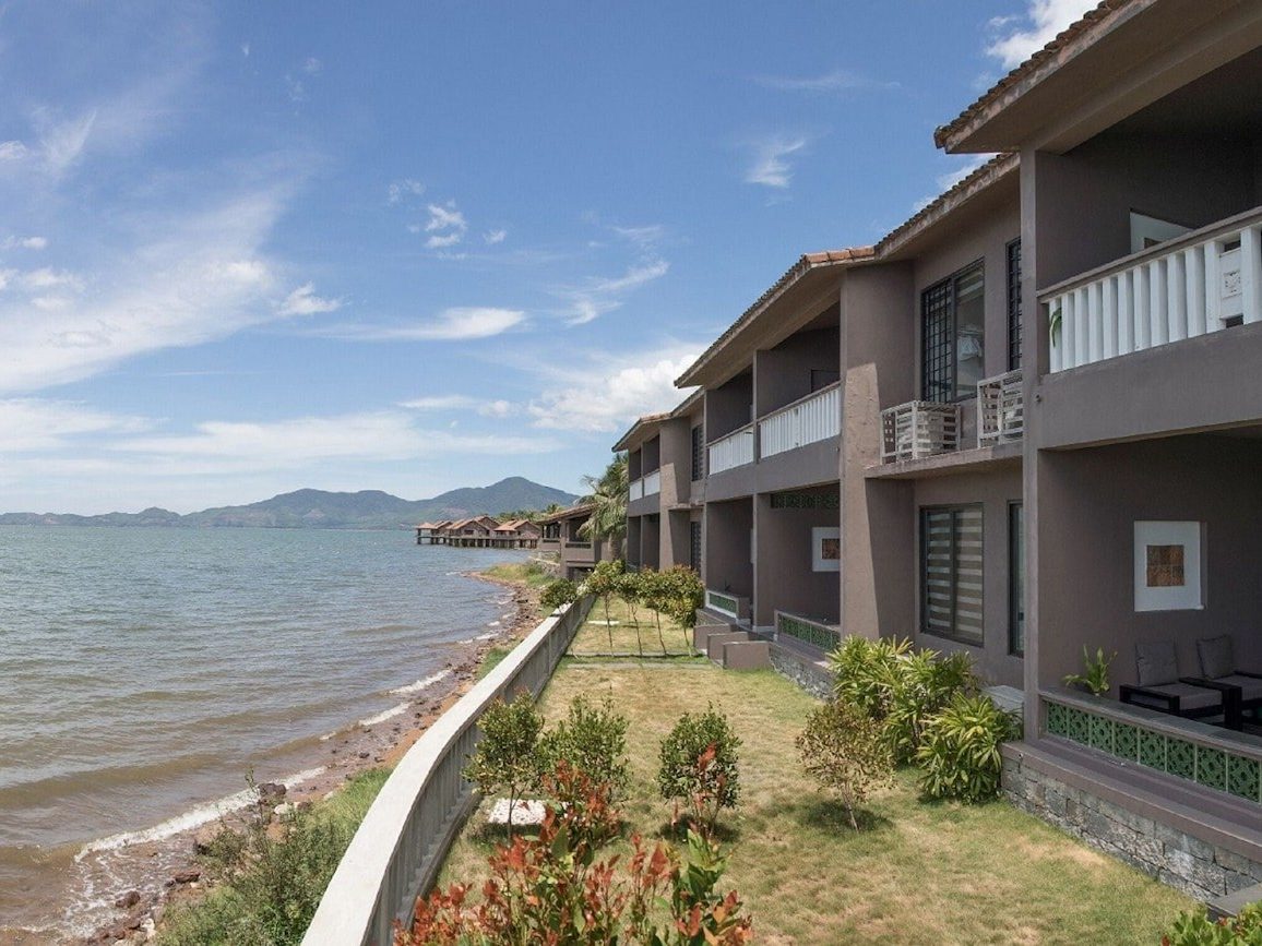 Two-story row of rooms with white balcony rails along a stone embankment at the water’s edge