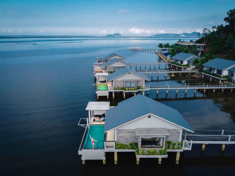 Over-water villa with slate-grey roof and a turquoise plunge pool on its deck, more villas and jetties behind