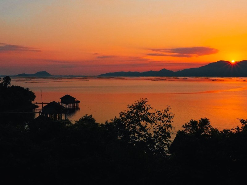 Sunset over a calm lagoon with dark hills and a small pavilion on the water
